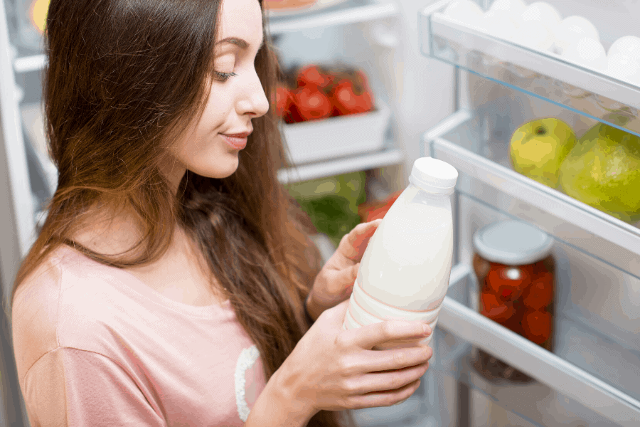 woman with brown hair checking expiration date on milk in front of refrigerator